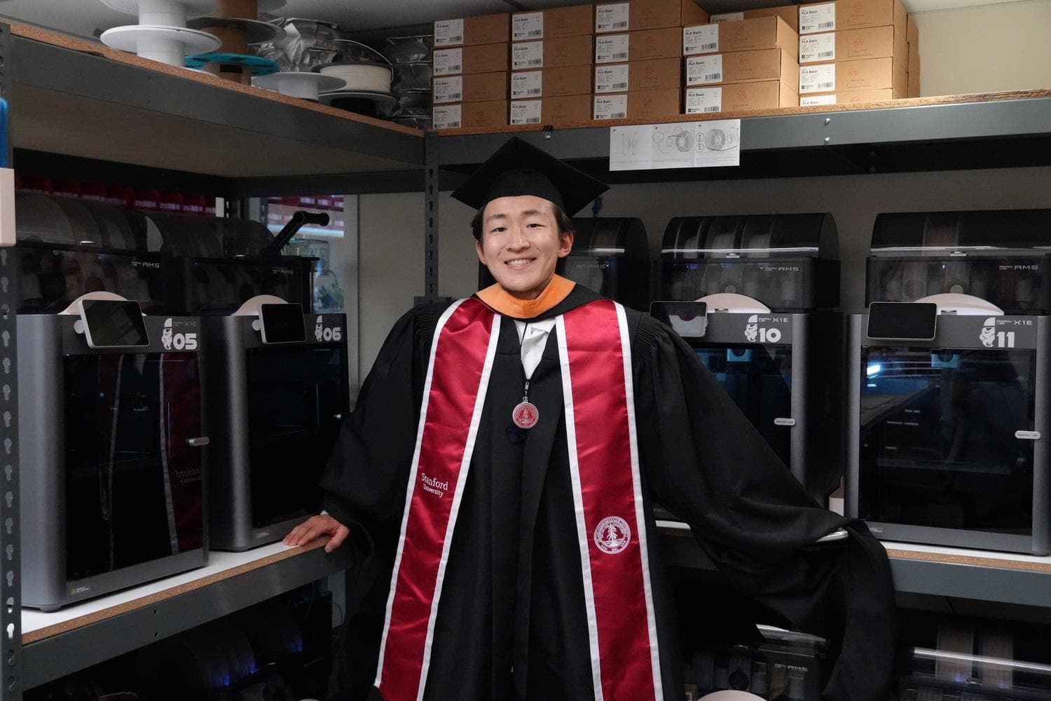 John in graduation robes inside a fabrication lab